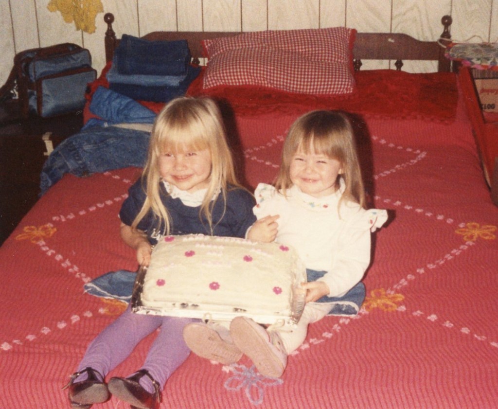 two young girls sitting on a bed, holding a cake